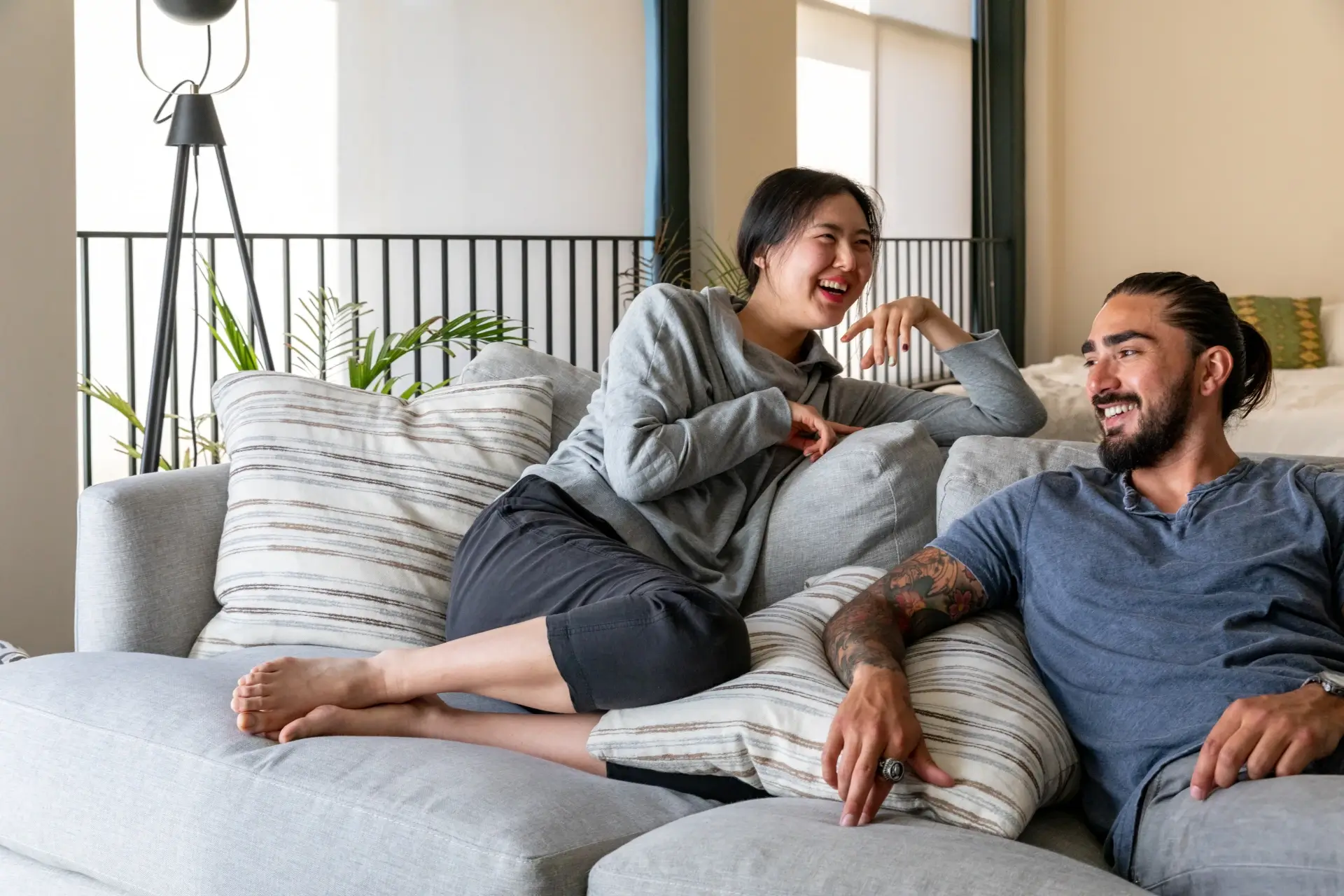 A relaxed biracial couple lounges on a plush couch in a brightly lit apartment